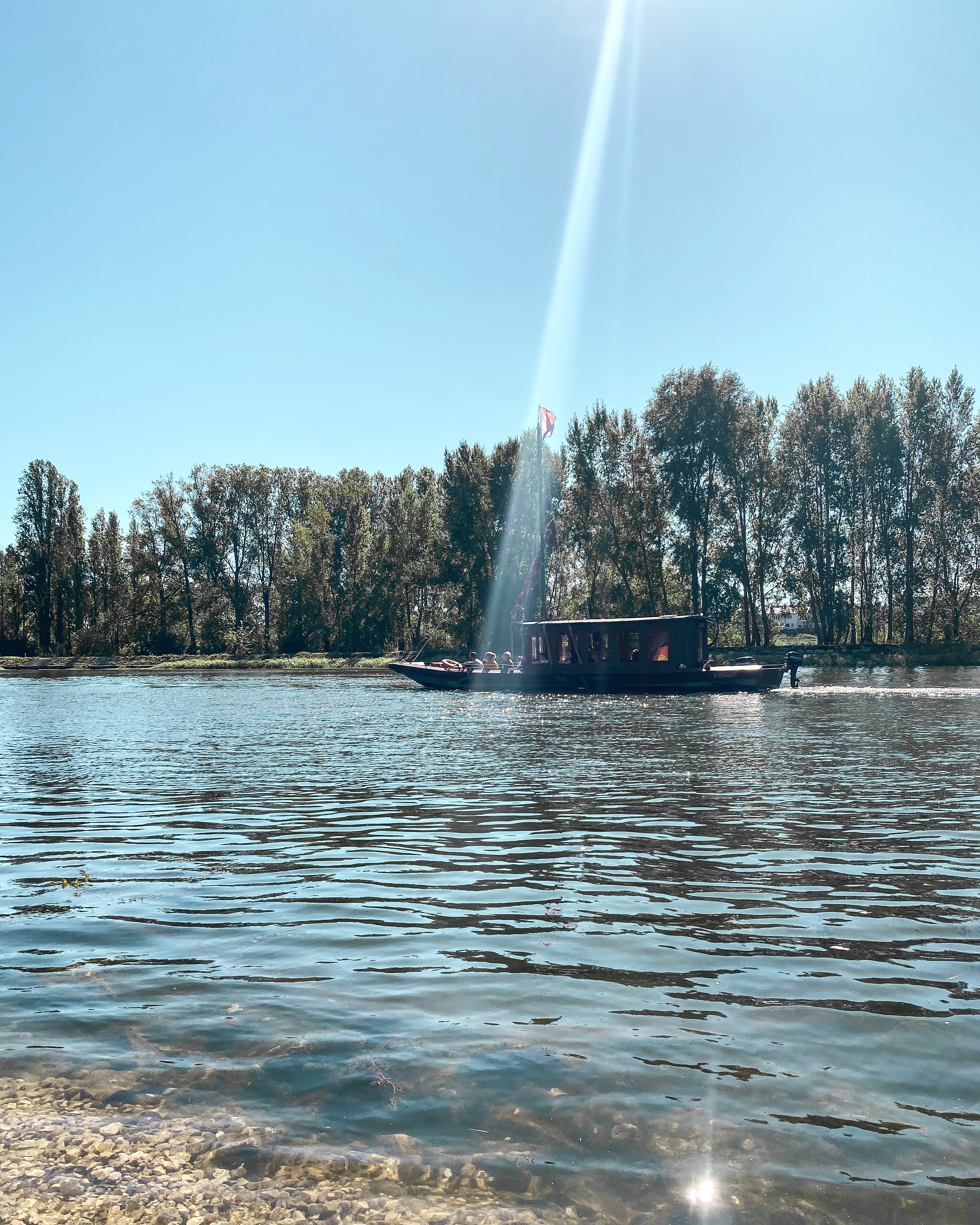La Loire prise au ras de l'eau ; un rayon de soleil tombe sur un bateau qui passe ; au fond des arbres