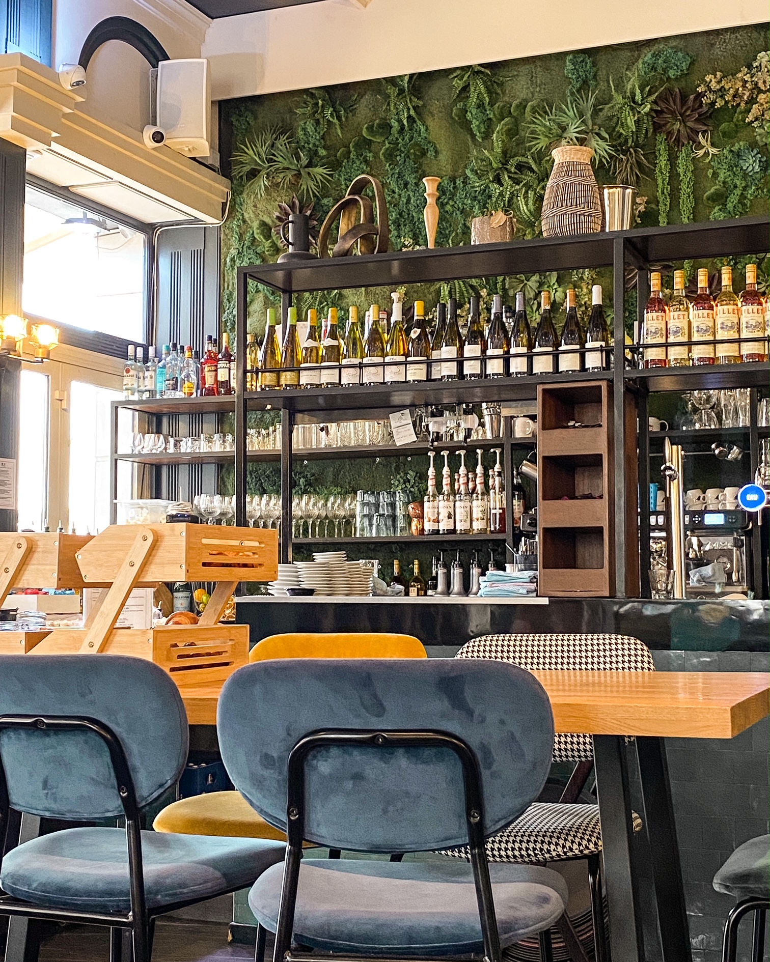 L'intérieur d'un café, au premier plan une table avec des chaises, au fond le bar