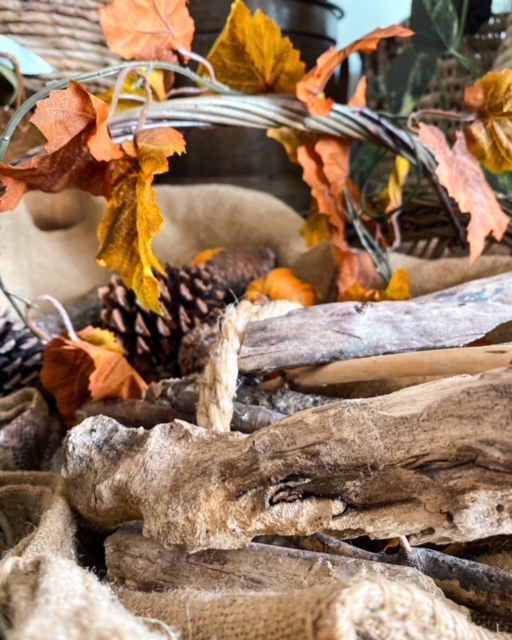 Un panier tressé contenant des morceaux de bois, des pommes de pain, une guirlande de fausses feuilles est attachée à l'anse