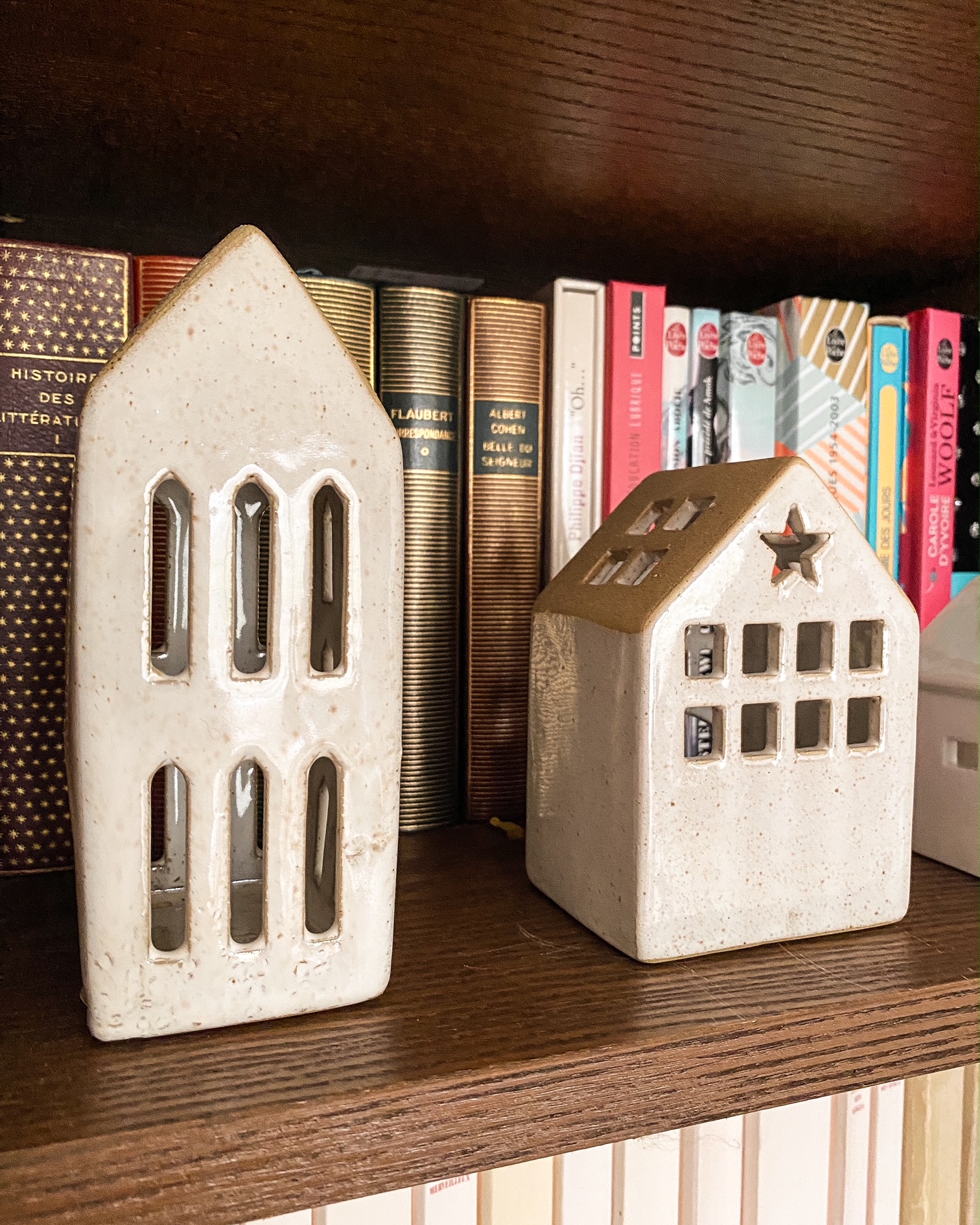 Deux petites maisons en céramique sur une étagère devant des livres