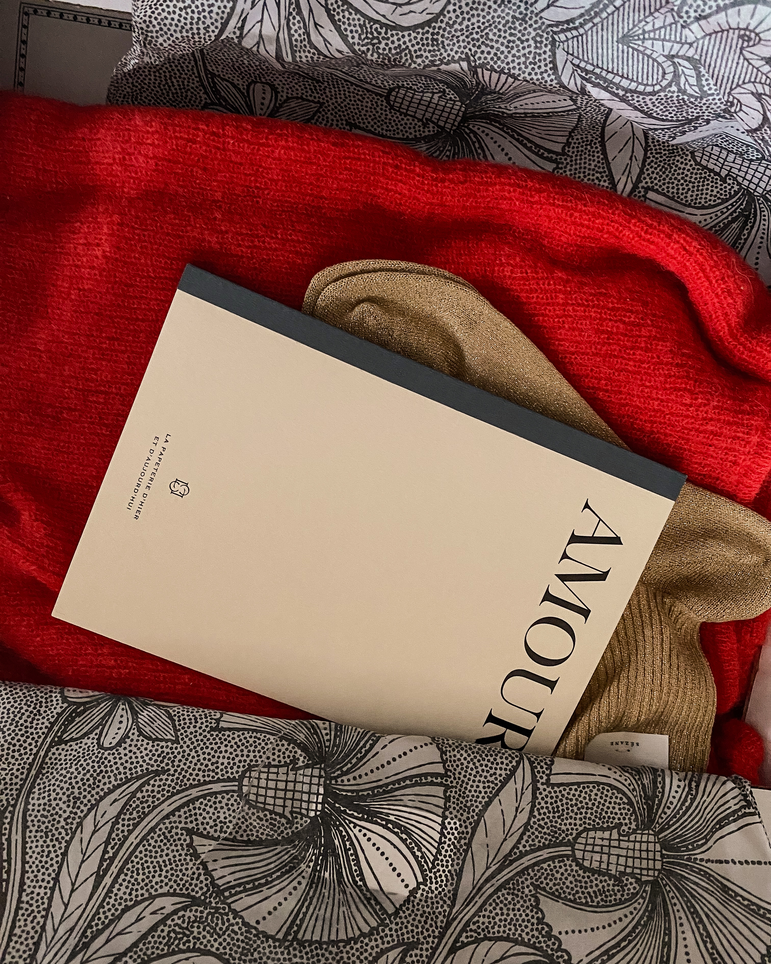 Un colis ouvert ; un pull rouge, des chaussettes dorées, un carnet Amour