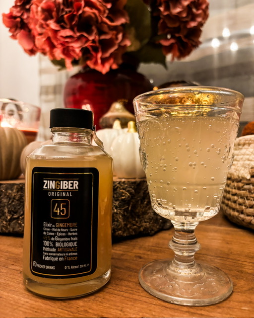 Un verre en cristal rempli d'une boisson pétillante, une petite bouteille de Zingiber